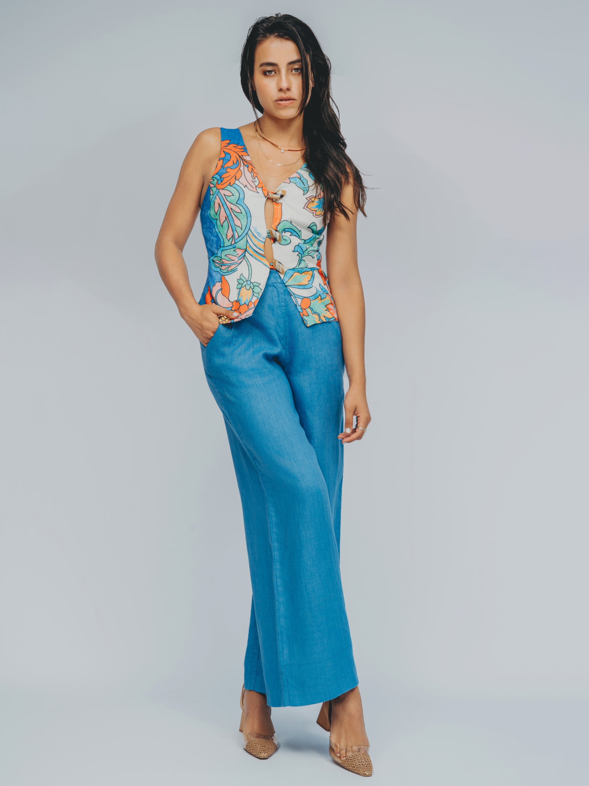 Woman wearing a colorful sleeveless top and blue pants on a gray background