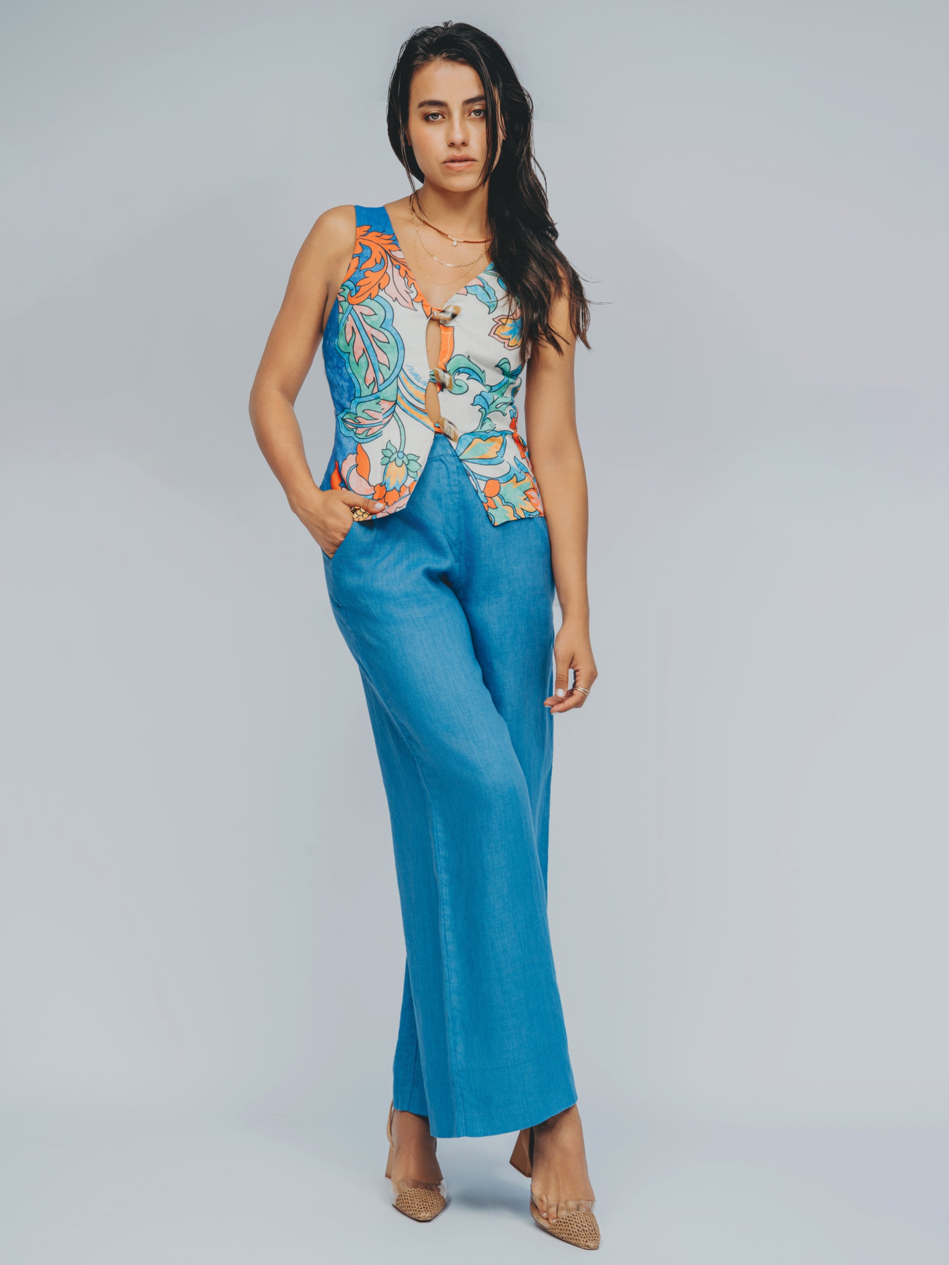 Woman wearing a colorful sleeveless top and blue pants on a gray background