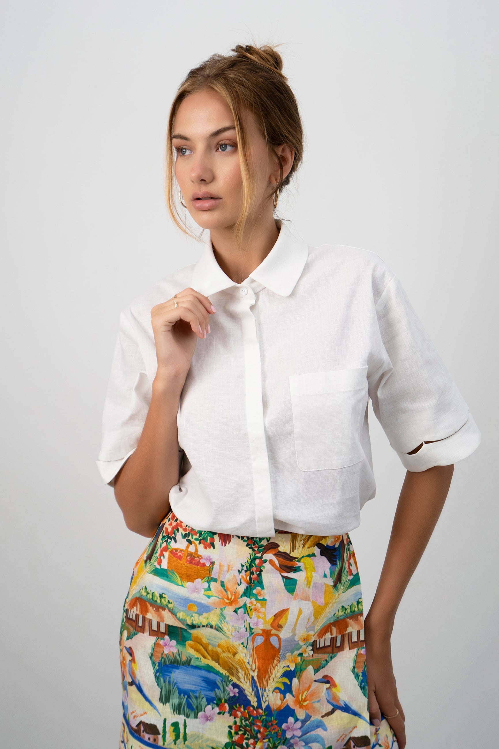 A model wearing the white Pilgrimage Shirt and the Halcyon Days Skirt asymmetrical faux wrap mini skirt featuring exclusive vibrant and picturesque textile print.