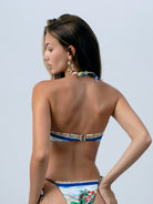Back view of of a model wearing a multicolored vibrant floral bikini, the Maize Bikini by Nina Apres Swim, with tie-side gold beads detail and back clip for closure.