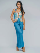 Woman wearing a colorful sleeveless top and blue pants on a gray background