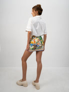 A model wearing the white Pilgrimage Shirt and the Halcyon Days Skirt asymmetrical faux wrap mini skirt featuring exclusive vibrant and picturesque textile print - back view shown.