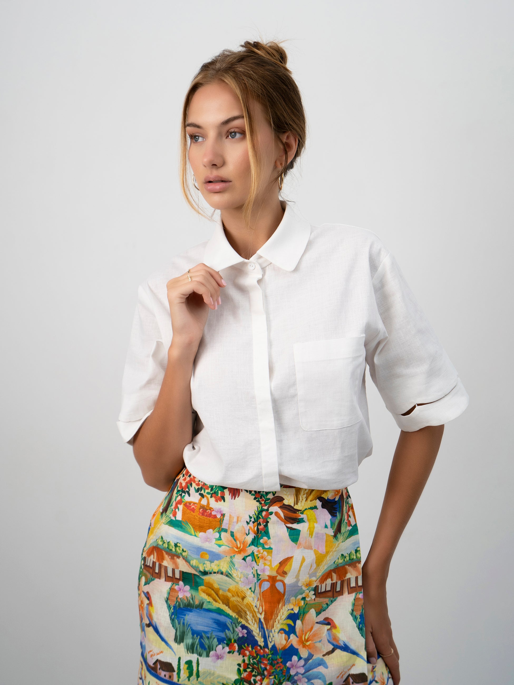 A model wearing the white Pilgrimage Shirt and the Halcyon Days Skirt asymmetrical faux wrap mini skirt featuring exclusive vibrant and picturesque textile print.