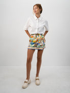 A model wearing the white Pilgrimage Shirt and the Halcyon Days Skirt asymmetrical faux wrap mini skirt featuring exclusive vibrant and picturesque textile print.