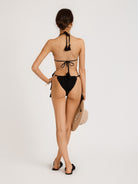Back view image of the INDIAN SUMMER TIE SIDE BRIEFS, a stylish and handcrafted swimwear piece from the Inherent Beauty collection. The model is showcased wearing black colour briefs and matching top, with tasseled side and back ties for easy adjustment.