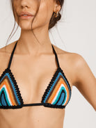 This image is a close up of the INDIAN SUMMER TRI TOP, a handcrafted swimwear piece from the Inherent Beauty collection. The model is showcased wearing the vibrant, multicolored top which is accented with black scallop-shaped edging.
